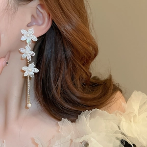 Detail of lily flower earring with pearl tassels and crystal accents on a model