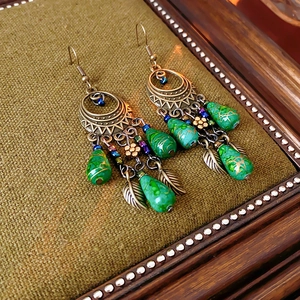 Detail view of retro bronze crescent earrings with green water drop beads and gold leaf accents