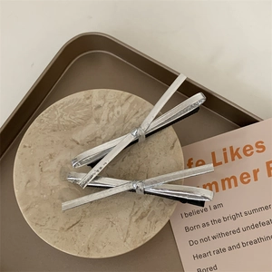 Detail of two silver metal knot hairpins on a marble tray with minimalist aesthetic