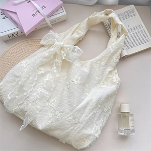 Detailed close-up of cream lace embroidery and floral patterns on the soft fabric handbag