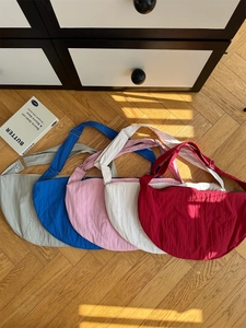 Detailed top view of five nylon crescent crossbody bags in various pastel colors on wood floor