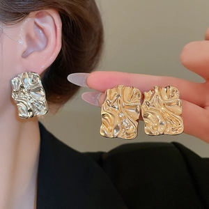 Detailed macro view of square crinkle textured metal stud earrings in gold and silver
