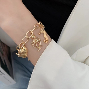 Detail of gold ocean charm bracelet with seahorse and shell pendants on wrist