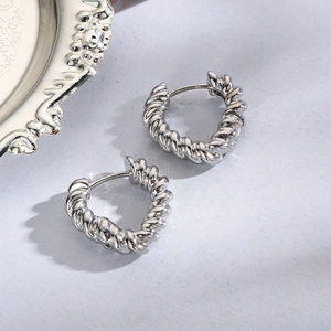 Detail of silver twisted hoop earrings with textured metal finish on a blue fabric background