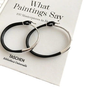 Minimalist S925 silver and black leather hoop earrings displayed on an art book cover