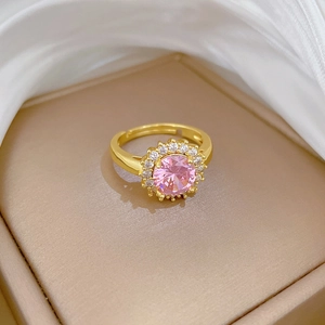 Vue macro d'une bague dorée ajustable avec pierre rose ronde et halo de diamants blancs