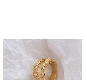 Close-up of golden wavy lava texture ring on white paper, minimalist jewelry detail