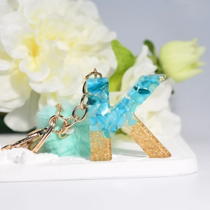 Close-up of resin letter K keychain with blue stones, gold foil and mint fur pompom
