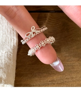 Close-up of silver bow and lace pearl rings showcasing intricate metal textures on fingers