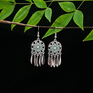 Detail of vintage silver earrings with green mandala pattern and leaf charms on wood