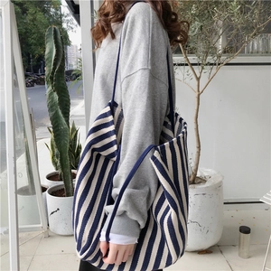 Side view of large striped canvas tote bag worn by model in a minimalist setting