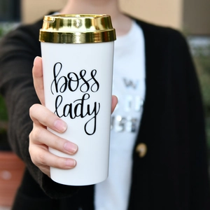 Close-up of hand holding a white Boss Lady insulated coffee mug with a gold lid