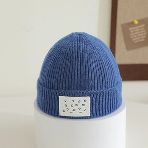 Close-up of blue ribbed knit beanie with white square patch showing artistic black letters