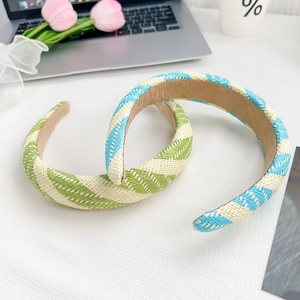 Braided candy-colored woven headbands in green and blue on a minimalist white desk setup