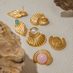 Retro gold earrings with pearls and green gems displayed on a natural stone surface