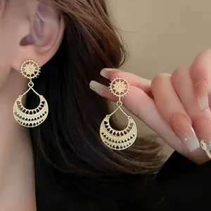 Detailed close-up of retro gold drop earrings with sunburst and hollow teardrop pattern