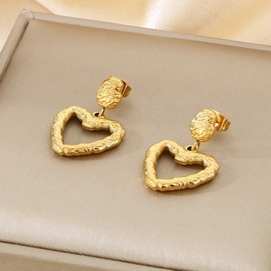 Macro detail of gold-plated heart earrings with a hammered texture on a gray jewelry box