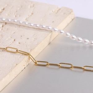 Detailed shot of pearl necklace and golden paperclip chain on stone background