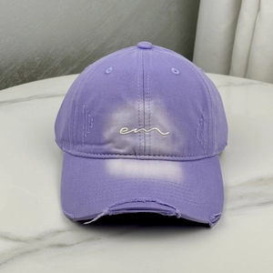 Close-up of purple baseball cap with white em embroidery and distressed frayed brim details