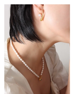 Detail of elegant imitation pearl drop earrings with minimalist golden metal hooks on a model
