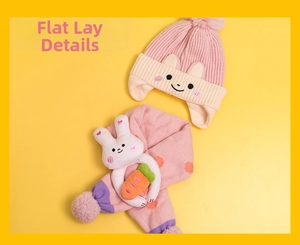 Flat lay of pink knit baby hat with rabbit embroidery and scarf with 3D bunny toy