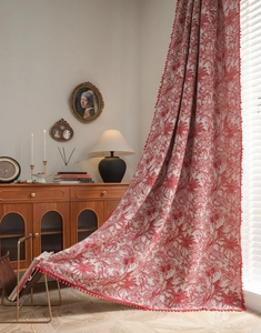 Detail of red floral curtains with plush pom-poms showing fabric texture and drape