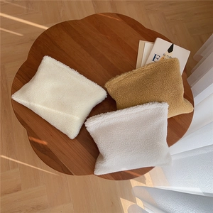Three plush lamb wool cosmetic bags in white and camel on a dark wooden table