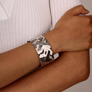Macro shot of silver wide wave-textured stainless steel cuff bracelet on model's wrist