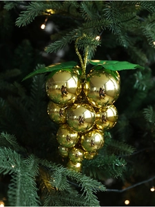 Detail of golden grape cluster Christmas ornament hanging on a lush green pine tree