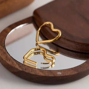 Polished 18K gold heart-shaped hoop earrings on a reflective wooden pedestal