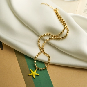 Detailed view of a gold beaded chain necklace with a yellow starfish pendant on fabric