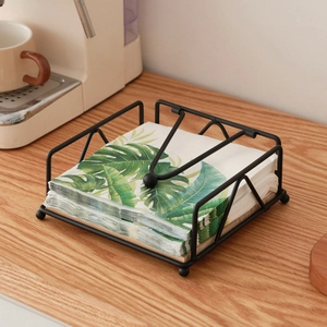 Modern black metal square napkin holder with weighted arm on wooden table for dining decor