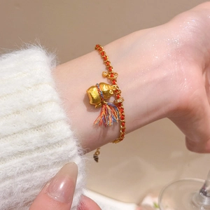 Détail d'un pendentif gourde plaqué or 24K sur un bracelet tressé rouge avec pompon en soie
