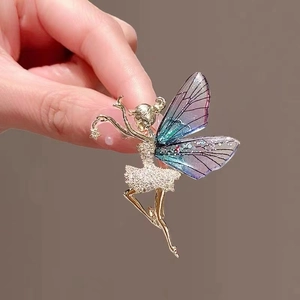Macro detail of fairy brooch with zircon wings and gold metal dress held by hand