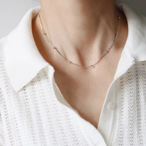 Close-up of a silver snake chain necklace with small beads worn on a neck