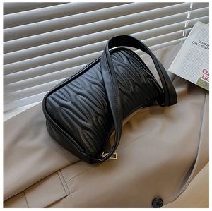 Top view of black quilted faux leather shoulder bag on a beige blazer with a magazine