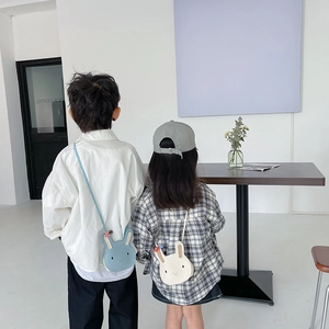 Rear view of children wearing cute 3D bunny coin purses in blue and cream colors
