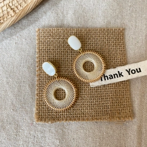 Detail of bohemian gold drop earrings with white stone and beige woven mesh pattern