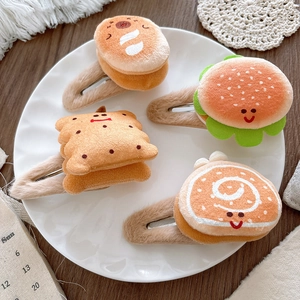 Close-up of plush cartoon hamburger and bread hair clips on a white ceramic plate