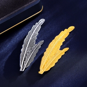 Elegant gold and silver feather-shaped metal brooches on premium dark blue fabric background