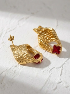 Detail of 18k gold conch-shaped earring with hammered texture and red zircon stone