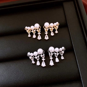 Detailed view of silver and gold pearl earrings with zircon teardrop charms on leather