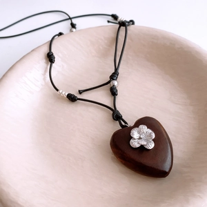 Detail of wooden heart pendant with silver flower inlay on black woven cord necklace