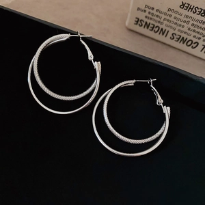 Close-up of layered silver hoop earrings with woven texture and smooth polished finish