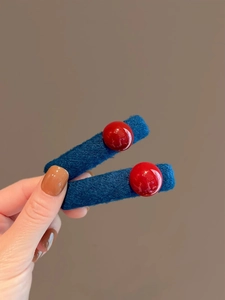 Detail of blue wool fabric hair clip with red bead accent held against a brown background