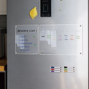 Macro detail of acrylic magnetic weekly planner and grocery list on a stainless steel fridge