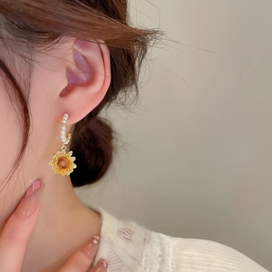 Detail of C-shaped pearl hoop earrings with yellow sunflower pendant worn by a model