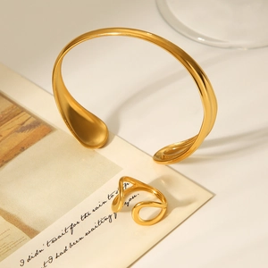 Detailed view of gold water-drop cuff bracelet and matching ring set on aesthetic background