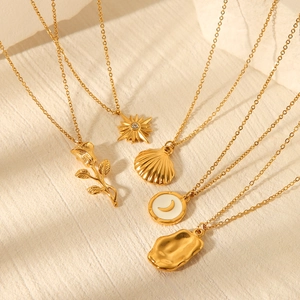 Flat lay of five gold necklaces featuring rose, sun, shell, and moon charms on beige surface
