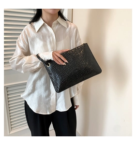 Detail of black crocodile texture envelope bag with gold hardware and wrist strap